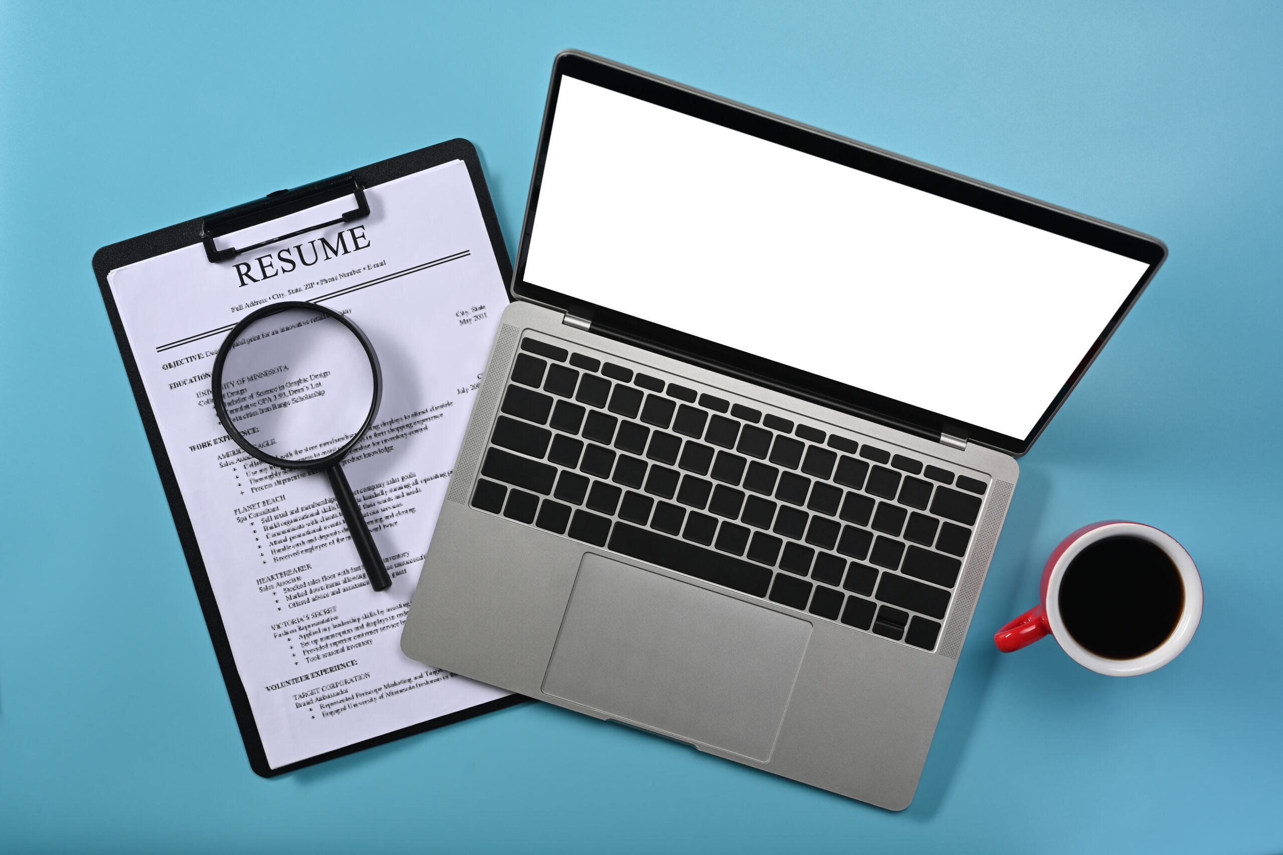 Above view laptop computer, magnifying glass and resumes applica