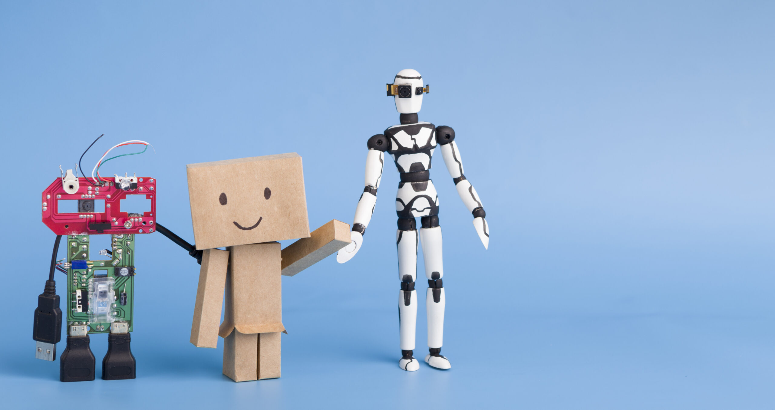 Three robots made with different materials on blue background, free space